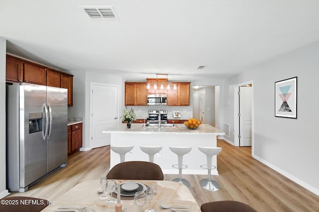kitchen featuring appliances with stainless steel finishes, light wood-style flooring, a kitchen island with sink, a kitchen breakfast bar, and brown cabinets