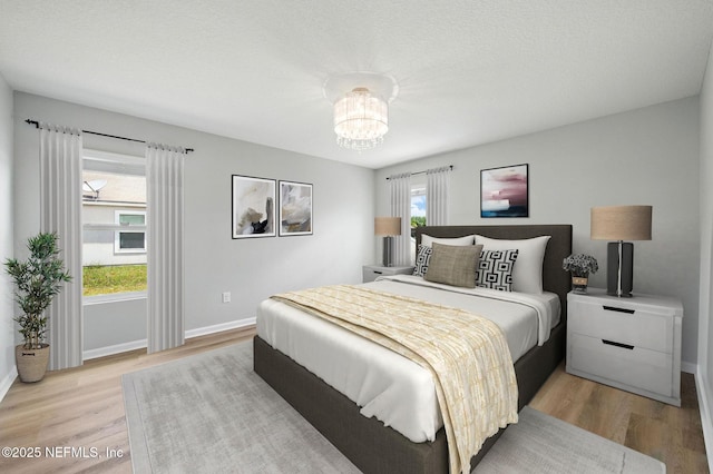 bedroom with light wood-type flooring, a chandelier, and baseboards