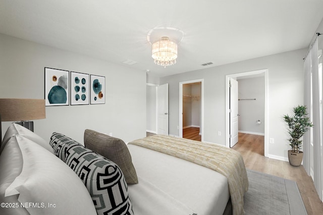 bedroom featuring a chandelier, light wood-style flooring, a walk in closet, baseboards, and a closet