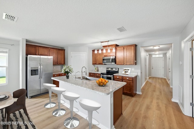 kitchen with stainless steel appliances, a sink, light wood-style floors, brown cabinets, and a breakfast bar