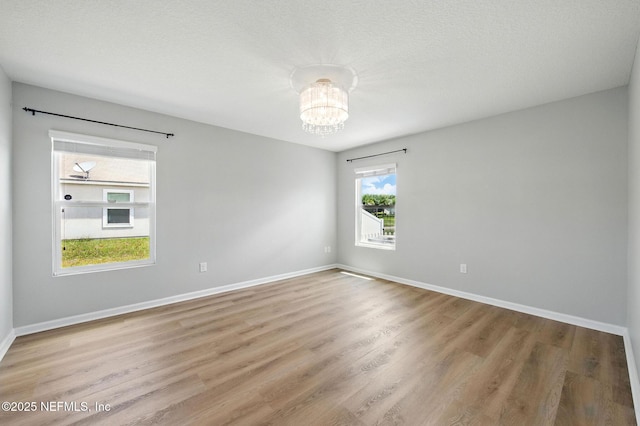 spare room featuring a chandelier, light wood-style flooring, and baseboards