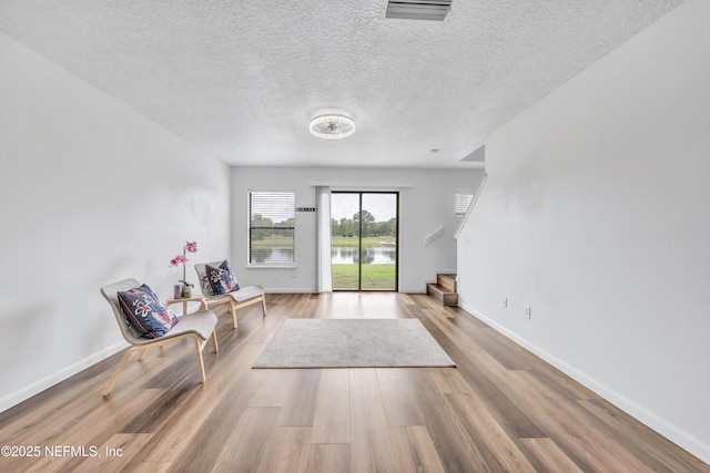 sitting room with wood finished floors, a textured ceiling, baseboards, and a water view