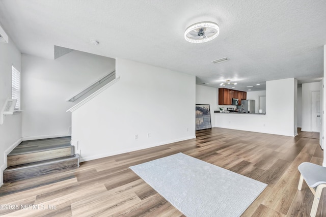 unfurnished living room featuring stairs, wood finished floors, a textured ceiling, and baseboards