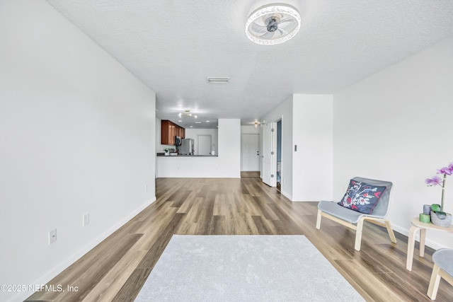corridor with wood finished floors, a textured ceiling, and baseboards