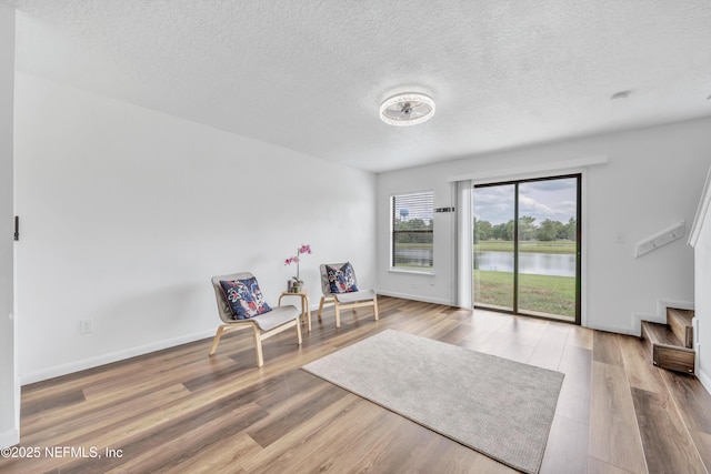 living area featuring wood finished floors, a textured ceiling, a water view, and baseboards