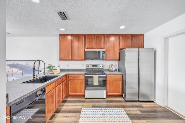 kitchen featuring stainless steel appliances, a sink, a textured ceiling, wood finished floors, and recessed lighting