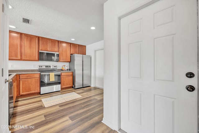 kitchen featuring stainless steel appliances, light wood-type flooring, recessed lighting, brown cabinetry, and light countertops