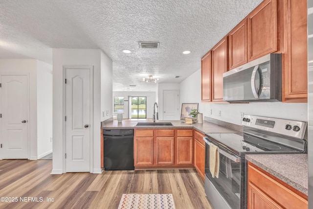 kitchen with stainless steel appliances, a sink, a textured ceiling, light wood finished floors, and brown cabinetry