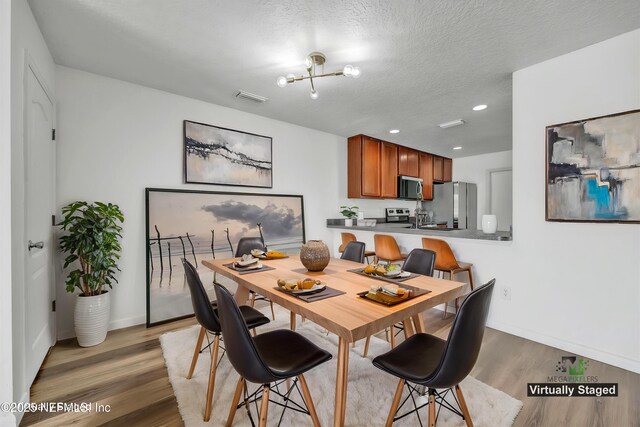 dining space featuring light wood finished floors, a chandelier, baseboards, a textured ceiling, and recessed lighting