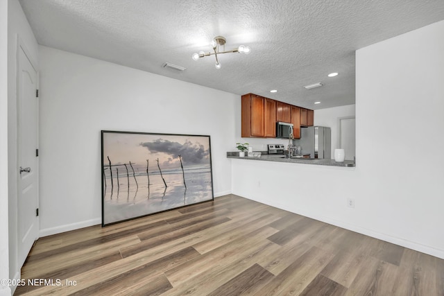 unfurnished living room featuring a textured ceiling, a chandelier, wood finished floors, recessed lighting, and baseboards