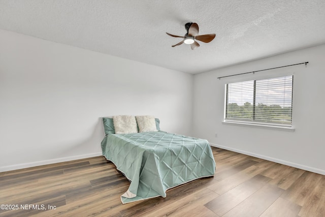 bedroom with a textured ceiling, baseboards, wood finished floors, and ceiling fan