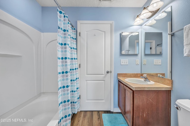 full bathroom with wood finished floors, vanity, shower / bath combo with shower curtain, toilet, and a textured ceiling