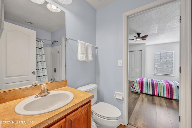 full bath with toilet, a ceiling fan, a textured ceiling, wood finished floors, and vanity