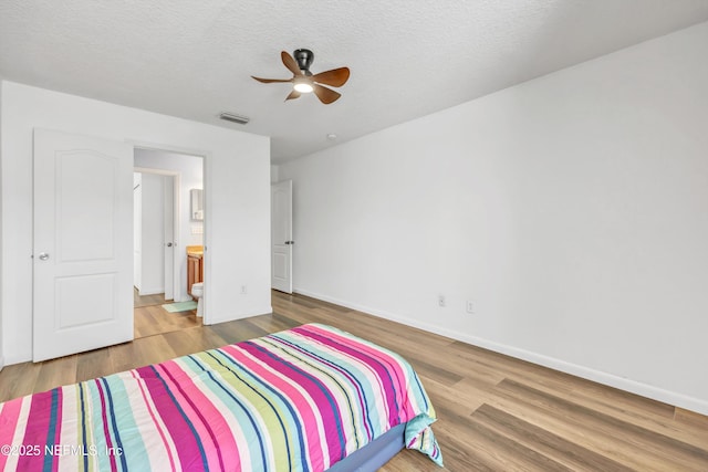 bedroom featuring wood finished floors, baseboards, a textured ceiling, ensuite bathroom, and ceiling fan