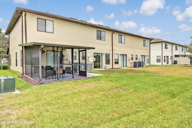 rear view of property featuring a lawn, a sunroom, stucco siding, and a patio area