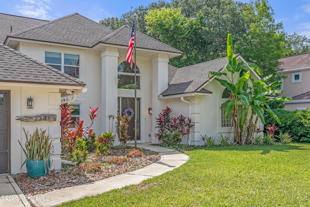 view of front of house featuring roof with shingles, stucco siding, and a front yard