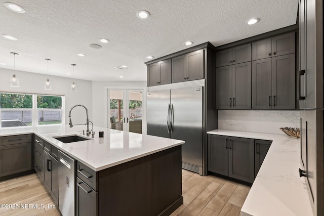 kitchen featuring stainless steel appliances, a sink, plenty of natural light, light wood-type flooring, and a textured ceiling