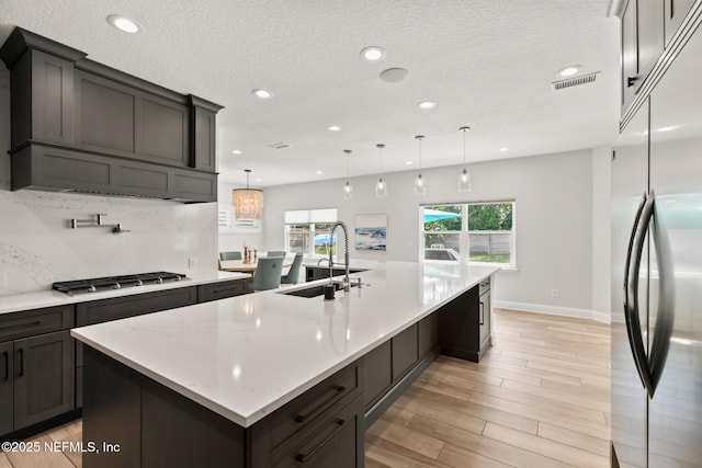 kitchen featuring stainless steel appliances, a sink, recessed lighting, a large island with sink, and light wood finished floors