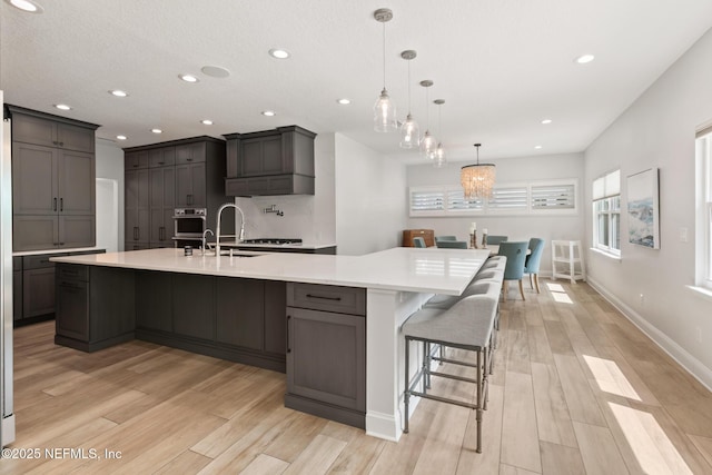 kitchen with a sink, light wood-type flooring, light countertops, a large island, and recessed lighting