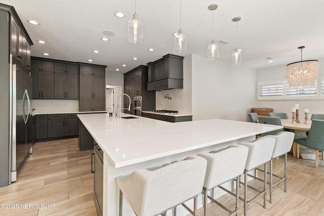 kitchen featuring stainless steel built in refrigerator, a sink, light wood-type flooring, a large island with sink, and recessed lighting
