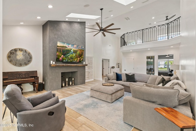living area with a skylight, recessed lighting, a towering ceiling, a ceiling fan, and wood finished floors