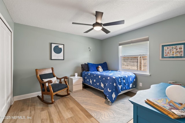 bedroom featuring wood finished floors, a closet, a textured ceiling, ceiling fan, and baseboards