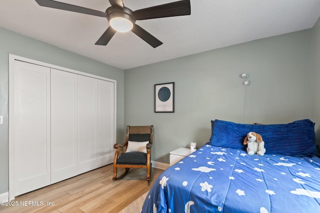 bedroom featuring light wood-style flooring, ceiling fan, a closet, and baseboards