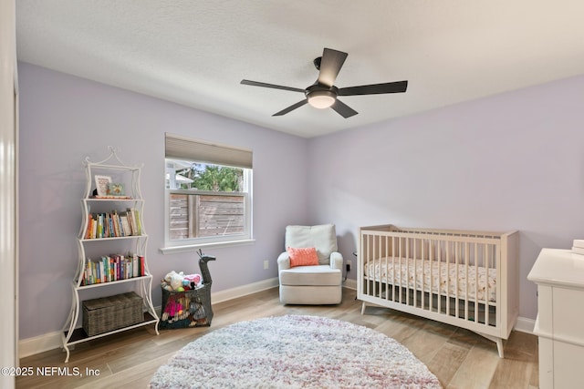 bedroom featuring wood finished floors, a nursery area, baseboards, and a ceiling fan