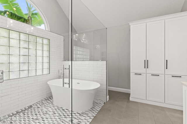 bathroom featuring a walk in shower, a freestanding tub, vaulted ceiling, tile patterned flooring, and baseboards