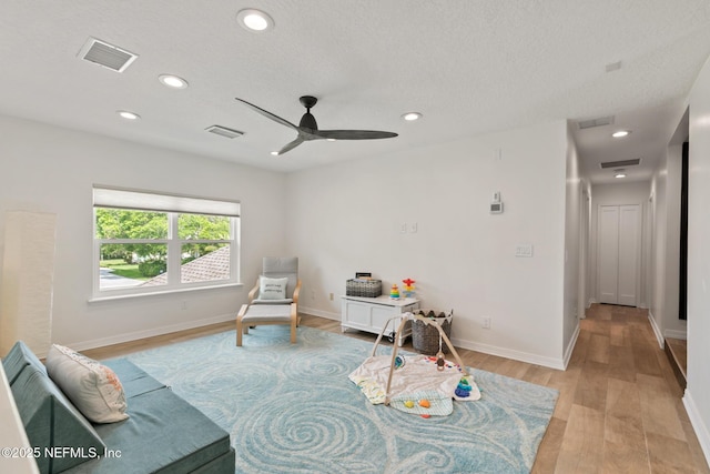 sitting room with light wood finished floors, a ceiling fan, recessed lighting, baseboards, and a textured ceiling
