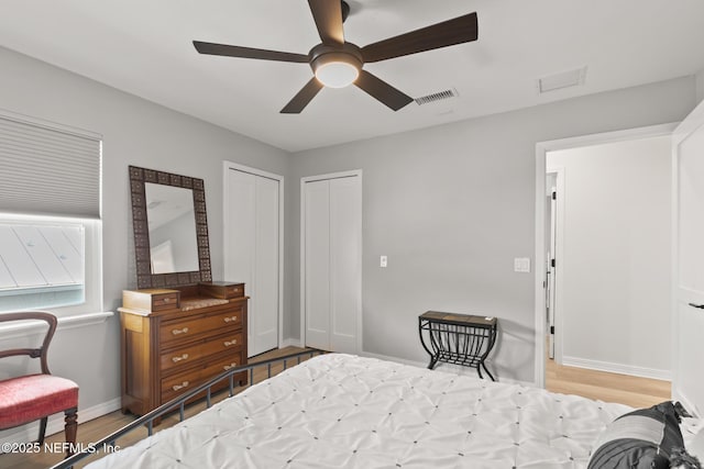 bedroom with wood finished floors, baseboards, ceiling fan, and multiple closets