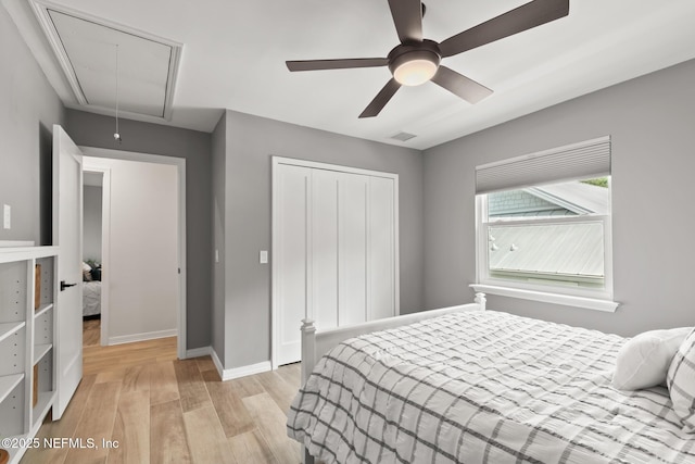 bedroom with attic access, light wood finished floors, a closet, baseboards, and ceiling fan