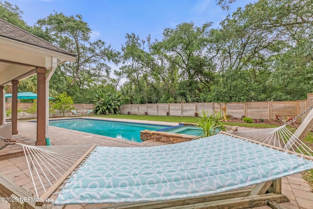 view of pool featuring a fenced backyard, a patio, view of scattered trees, and a pool with connected hot tub