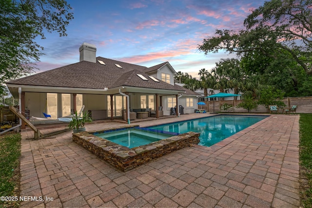 pool at dusk with a patio area, a fenced backyard, an outdoor hangout area, and a pool with connected hot tub