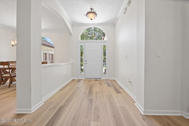 entrance foyer with wood finished floors, a textured ceiling, ornamental molding, baseboards, and arched walkways