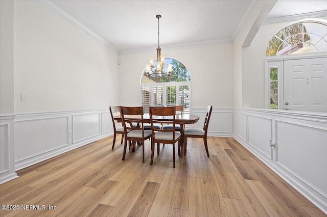 dining room featuring a chandelier, light wood-style floors, ornamental molding, wainscoting, and a decorative wall