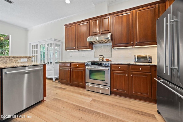 kitchen with stainless steel appliances, under cabinet range hood, ornamental molding, backsplash, and light wood finished floors