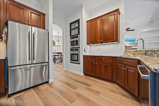 kitchen with appliances with stainless steel finishes, a sink, decorative backsplash, ornamental molding, and light wood finished floors