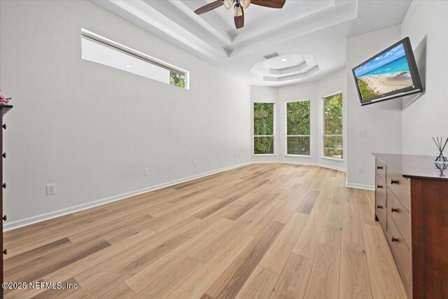 unfurnished living room with a tray ceiling, light wood finished floors, a ceiling fan, and baseboards
