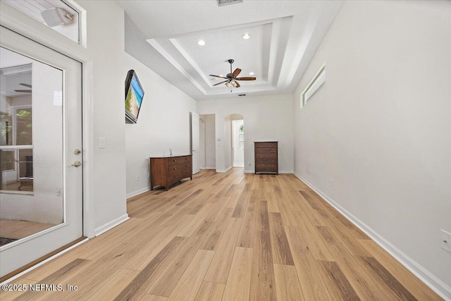 unfurnished living room with a raised ceiling, a ceiling fan, light wood-style flooring, recessed lighting, and arched walkways