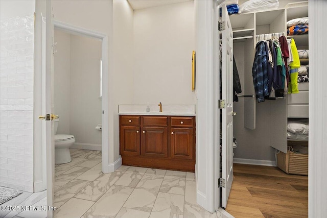 full bathroom featuring marble finish flooring, toilet, baseboards, a spacious closet, and vanity