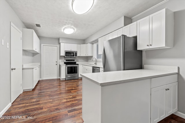 5092 Harvey Grant Rd, Fleming Island, FL 32003 - kitchen with stainless steel appliances, a peninsula, a textured ceiling, dark wood-style flooring, and white cabinetry
