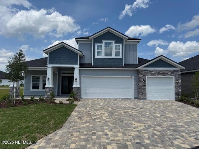 craftsman house with stone siding, decorative driveway, a front lawn, and an attached garage