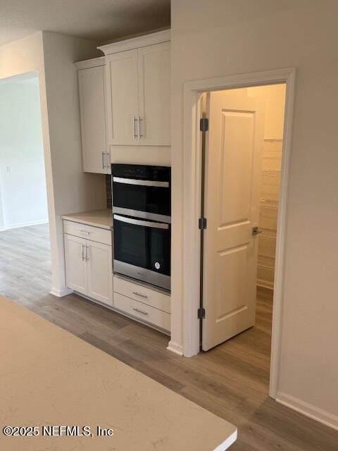 kitchen with wood finished floors, white cabinetry, light countertops, and baseboards