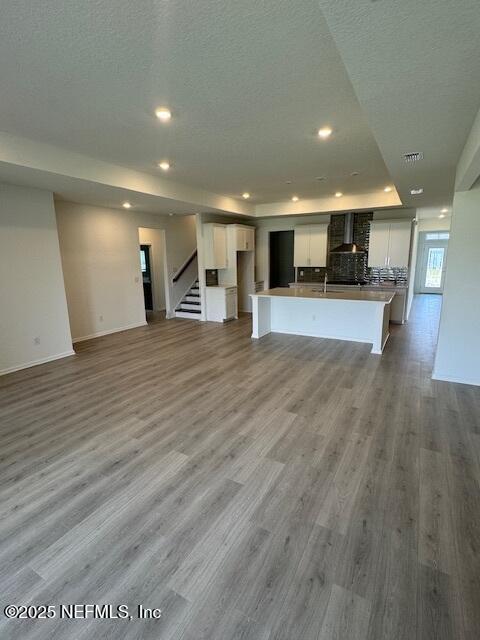 unfurnished living room featuring wood finished floors, recessed lighting, stairs, baseboards, and a textured ceiling