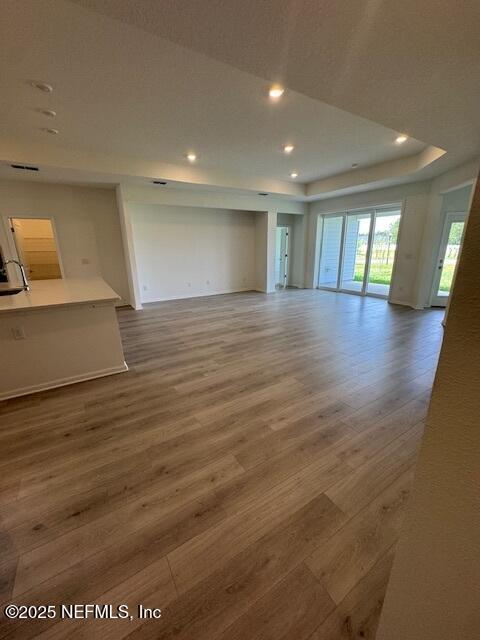 unfurnished living room featuring wood finished floors, recessed lighting, a raised ceiling, and baseboards