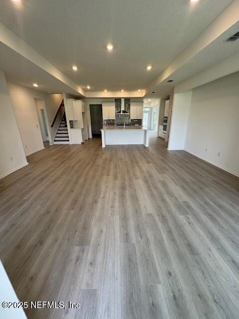 unfurnished living room featuring recessed lighting, wood finished floors, stairs, baseboards, and a tray ceiling