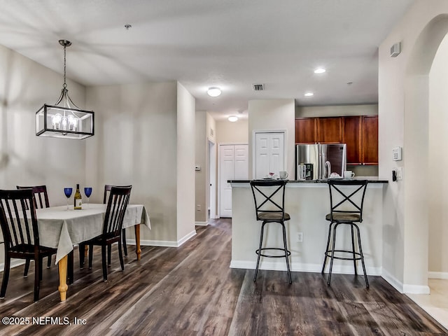 kitchen featuring stainless steel refrigerator with ice dispenser, brown cabinetry, a peninsula, dark countertops, and a breakfast bar