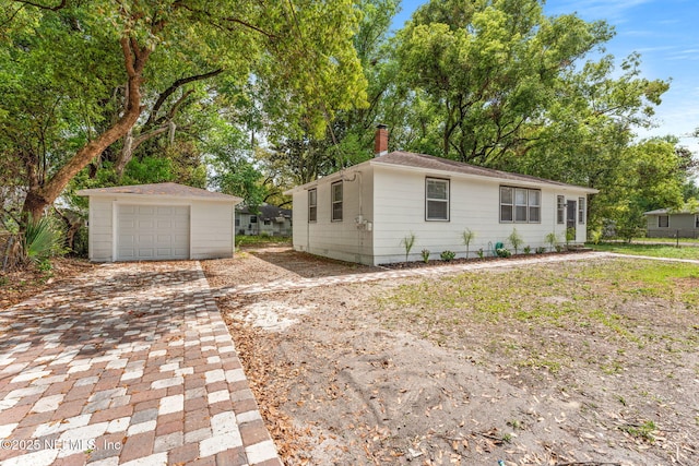 view of front of property with decorative driveway, a garage, an outbuilding, and a chimney