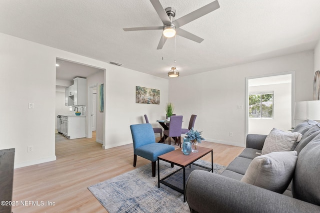 living room with light wood finished floors, a ceiling fan, a textured ceiling, and baseboards
